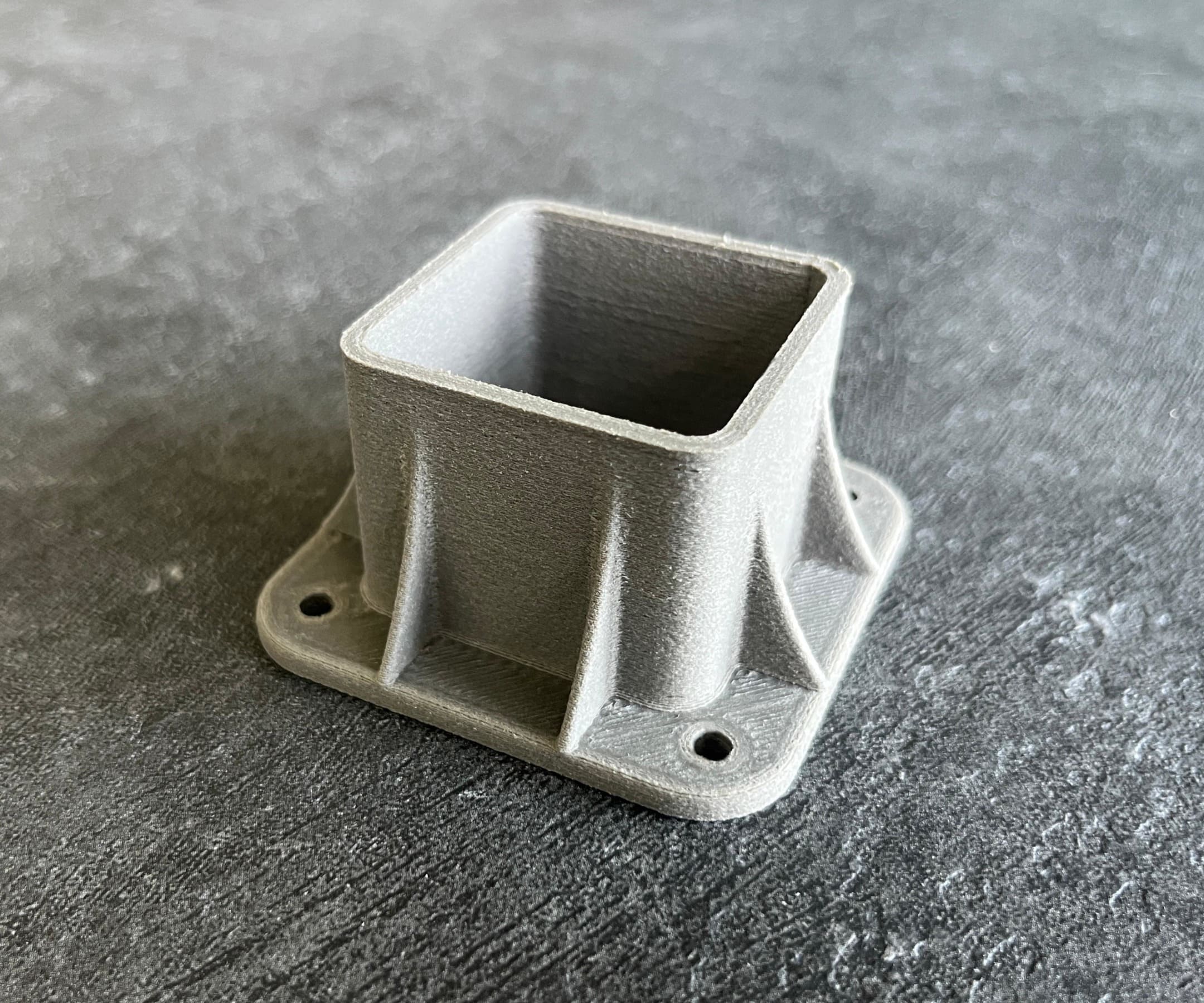 Graues FDM-3D-Druck Kunststoff-Bauteil in quaderförmiger Bauweise mit Flansch und Befestigungslöchern
